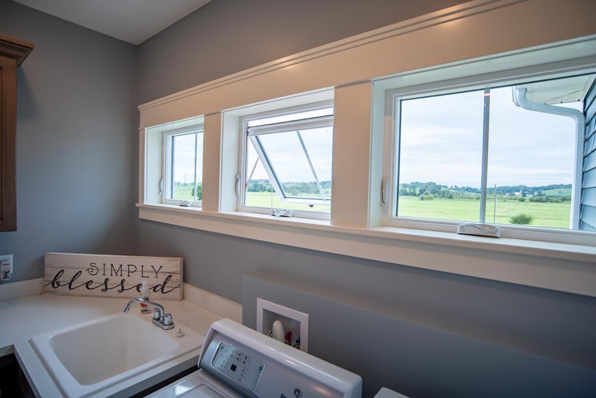 Laundry room with utility sink and washing machine, wooden Simply Blessed sign on wall, and large windows overlooking rural farmland